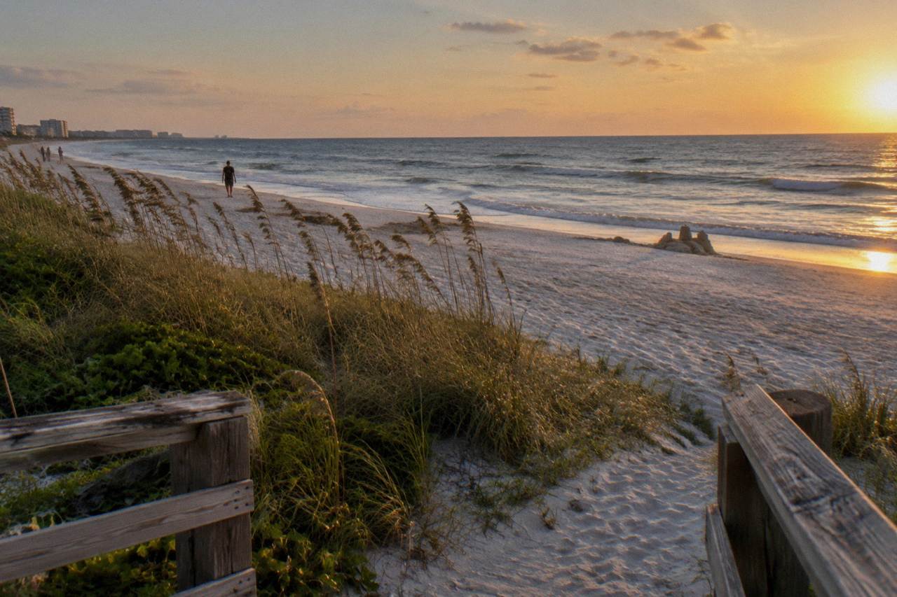 Wide view of a calm Cocoa Beach shoreline at golden hour with gentle surf and dune grass